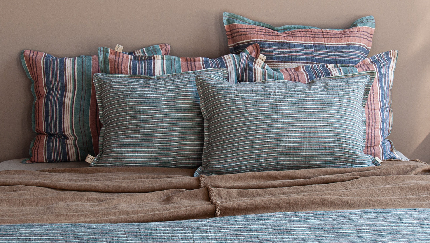 Cojines de lino en cama con colcha terracota y pie de cama verde rayado.
