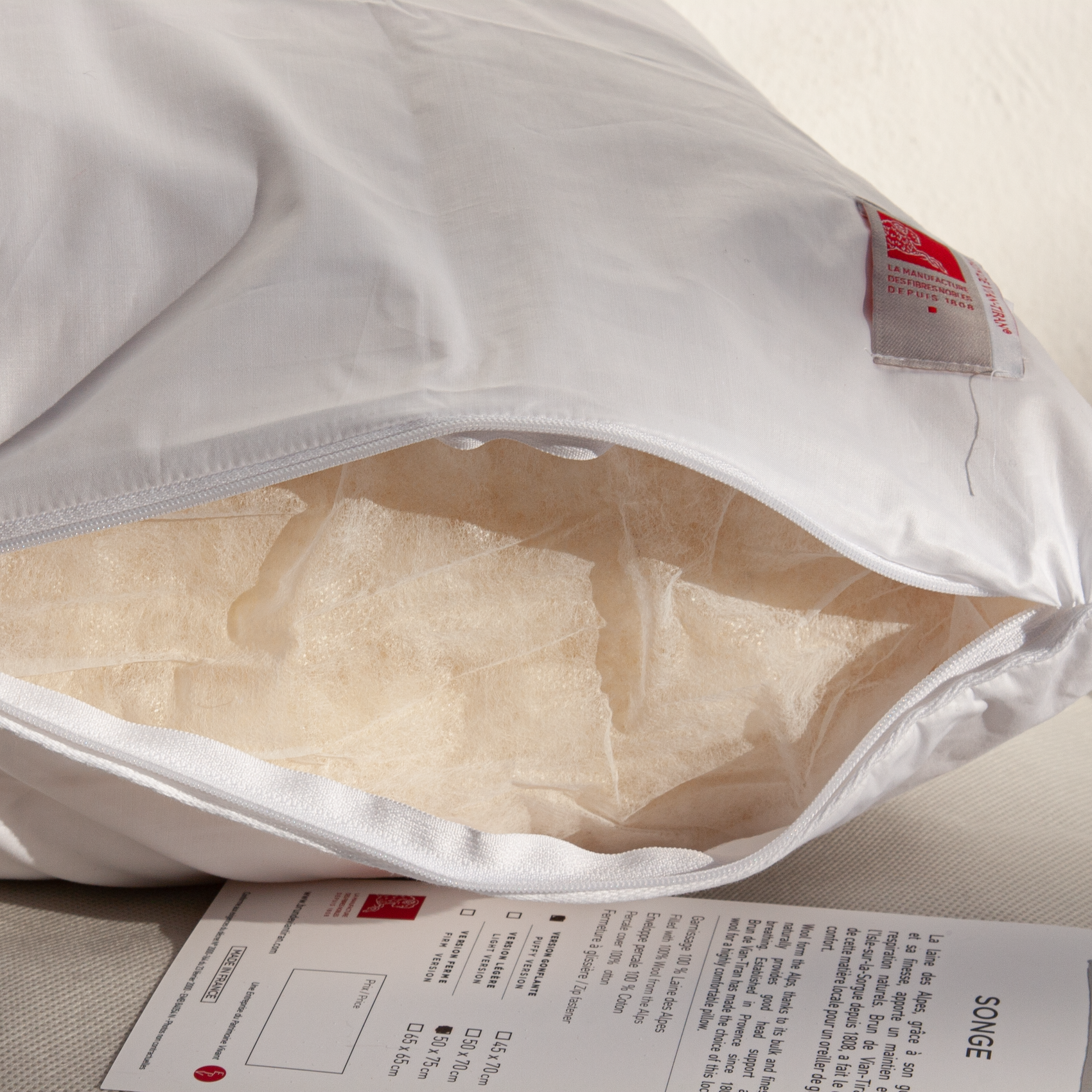 Primer plano del relleno de lana natural de los Alpes en almohada dELENZO, mostrando la fibra transpirable y elástica con sello Woolmark.