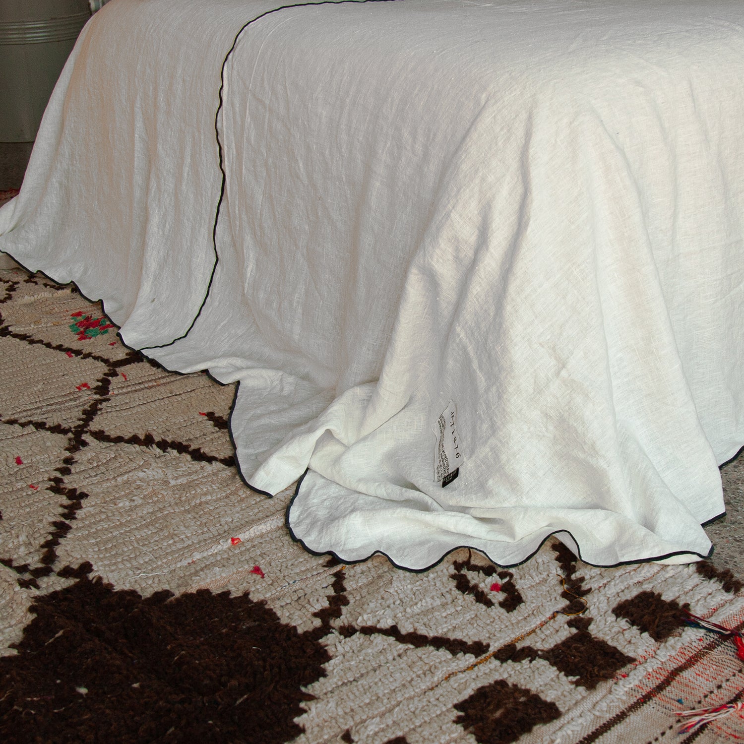 detalle de colcha blanca de lino con vivo de color negro sobre alfombra de lana natural.