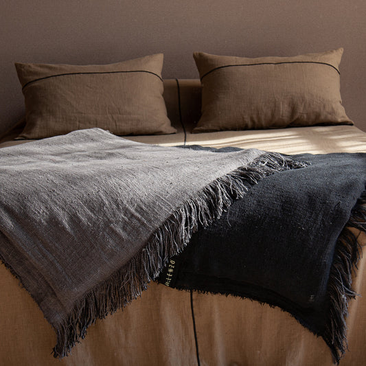 Vista de 2 Edredones para pie de cama bicolor con flecos sobre colcha de lino marrón.