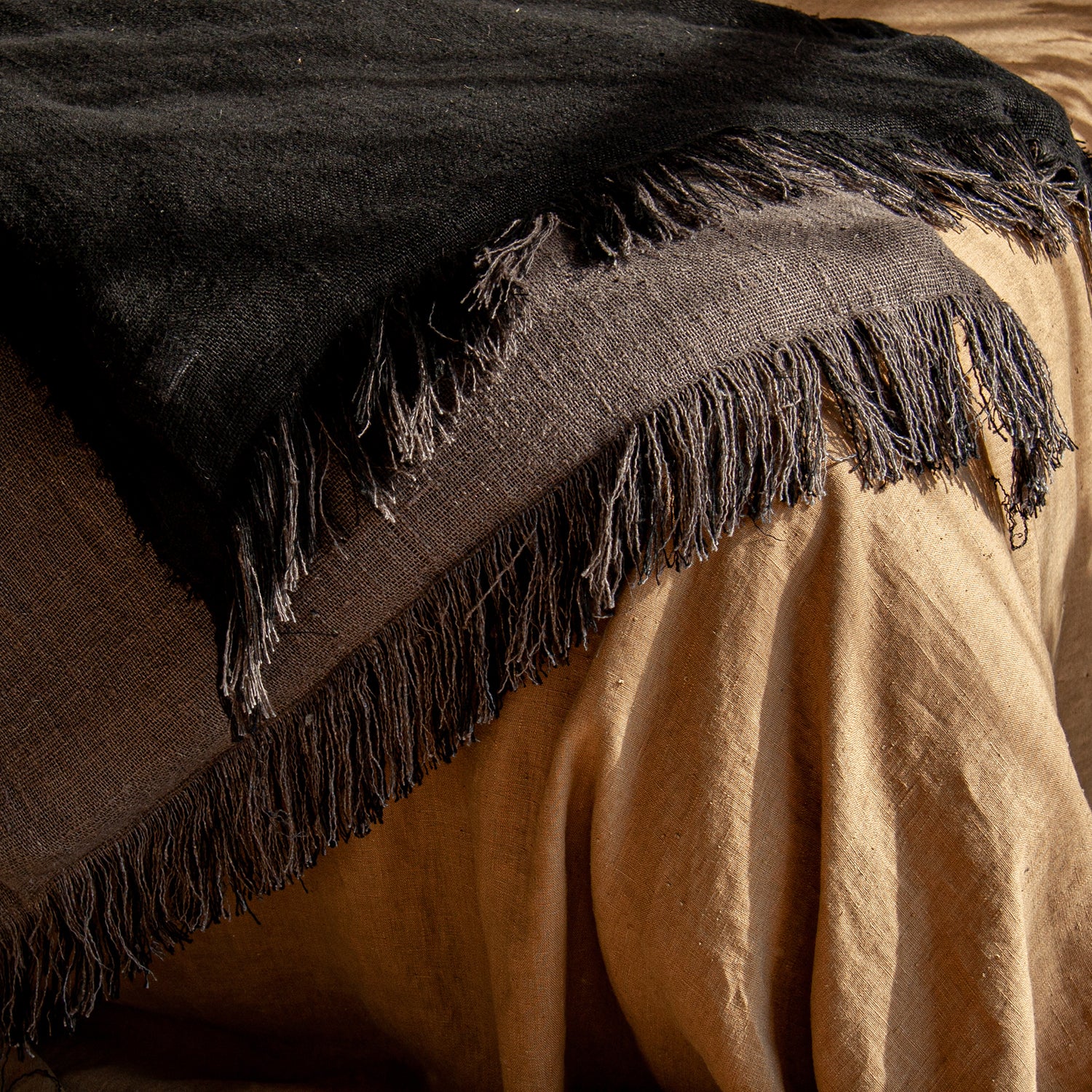 Edredones para pie de cama bicolor con flecos sobre colcha de lino marrón.