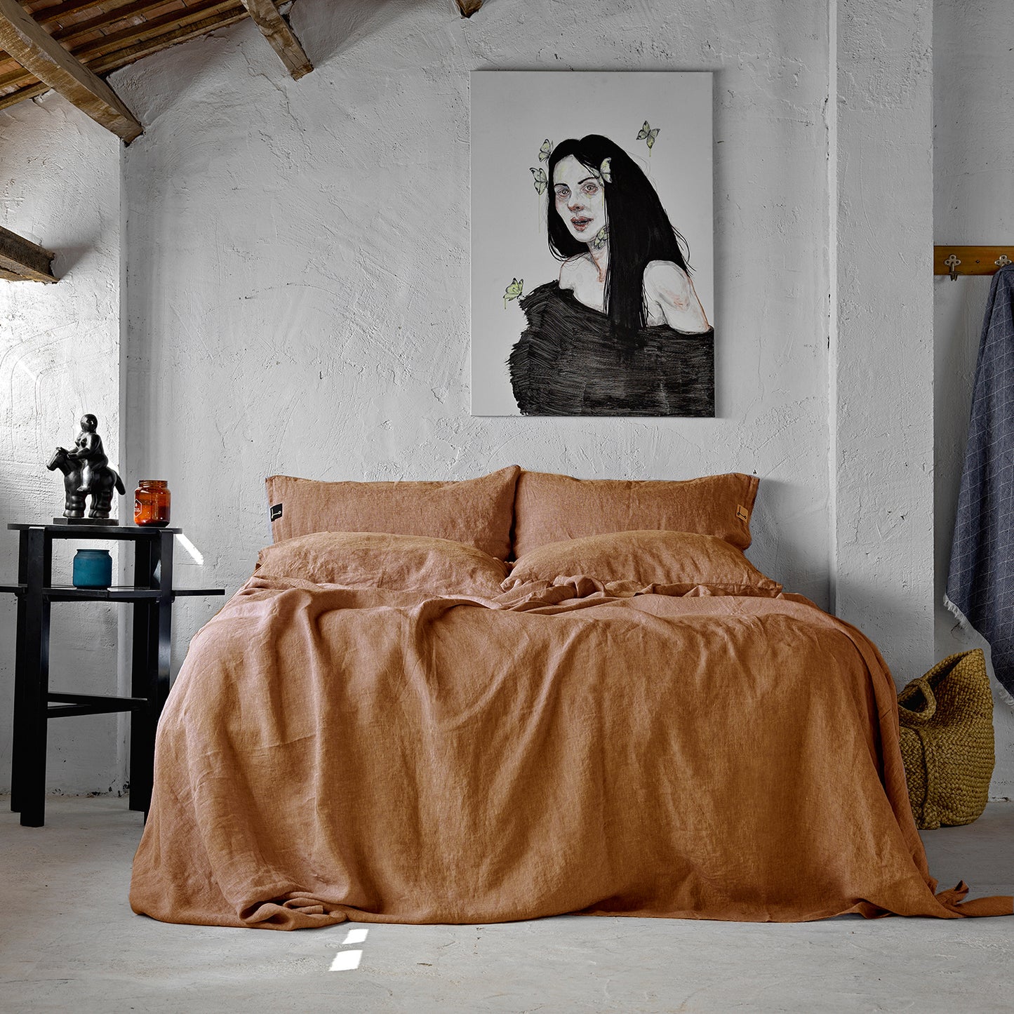 Cama de lino teja sobre suelo de cemento y paredes rústicas. Cuadro de Elena LLorens