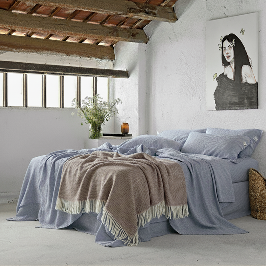 Juego de sábanas de lino lavado en una cama con ventanas altas y cuadro