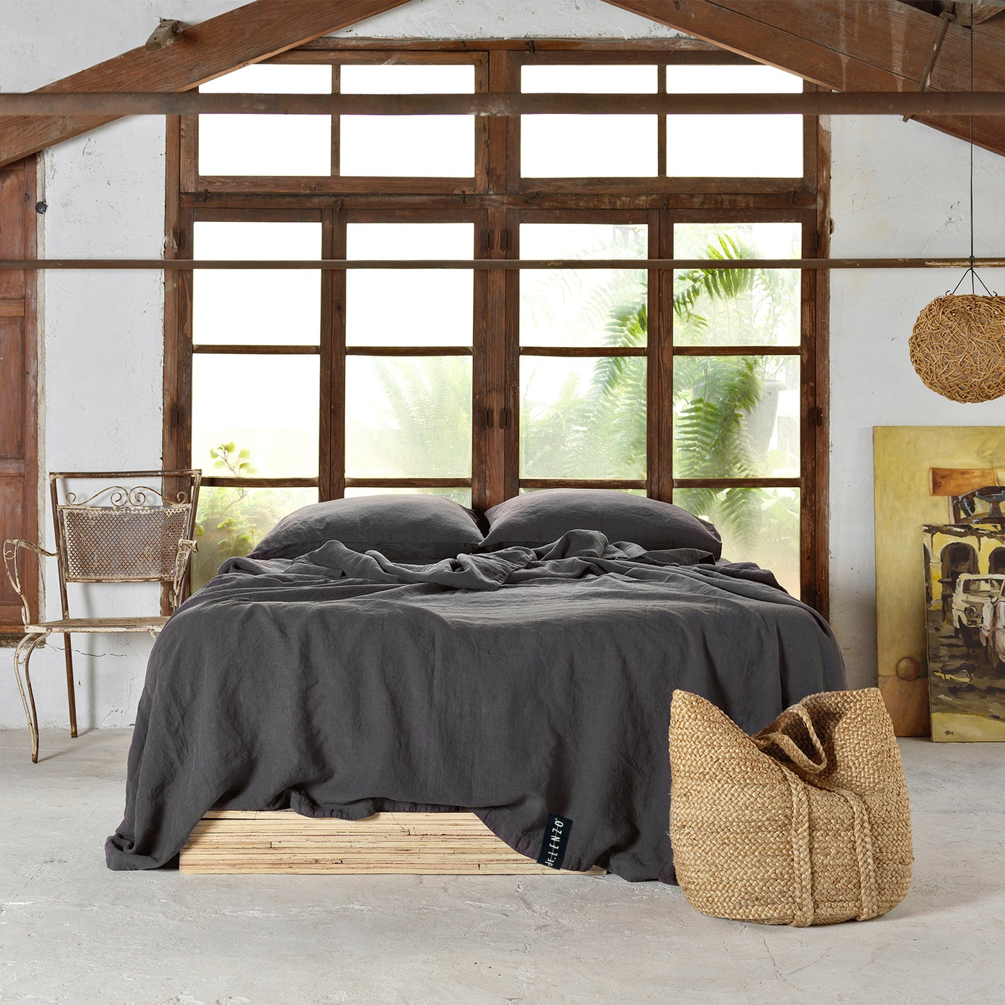 Cama en habitación de madera, con techo acuchillado. Juego de sábanas de lino gris oscuro.