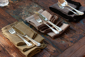Servilletas de lino de varios colores en mesa de madera y cubiertos de plata.