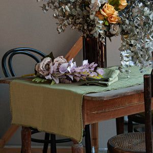 Imagen del camino de mesa verde con flores secas. Verde olivo y sus servilletas.