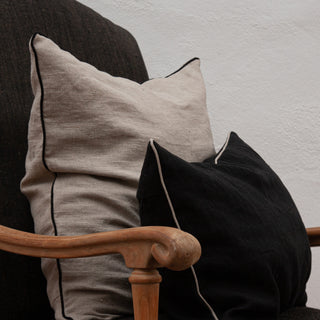 Detalle de Cojín de lino natural con borde de color negro. Dos cojines en sillón de lino rústico.