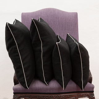Cuatro cojines de lino negro con reborde natural en sillón de lino morado.