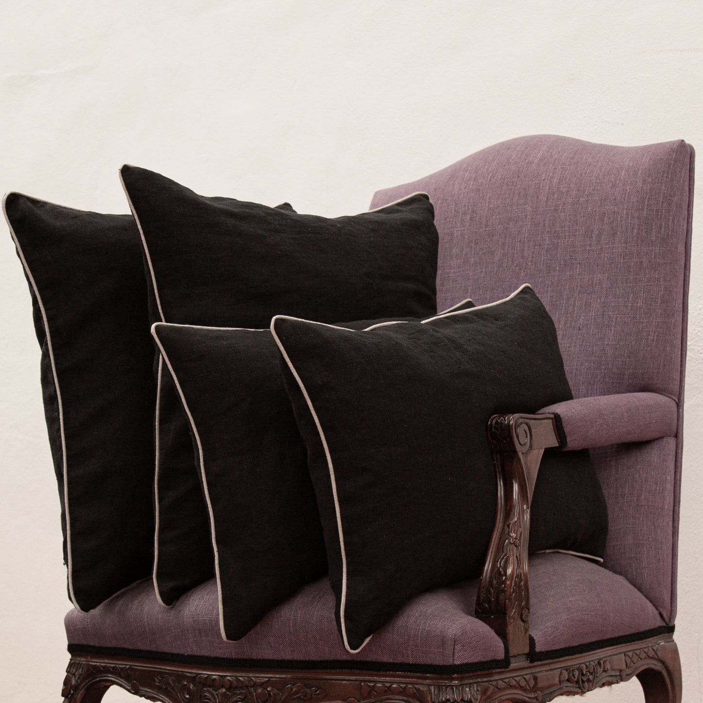 Cojines de lino negro con borde de lino natural. Grupo de varios tamaños en sillón de lino morado.