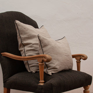 Cojín de lino natural con borde de color negro. Dos cojines en sillón de lino rústico.