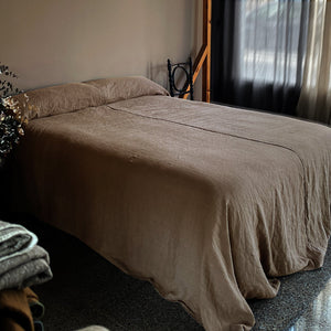 Colcha de lino terracota con cortinas grises.