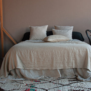 Colcha de lino de color arena, sobre cama vestida de lino natural.
