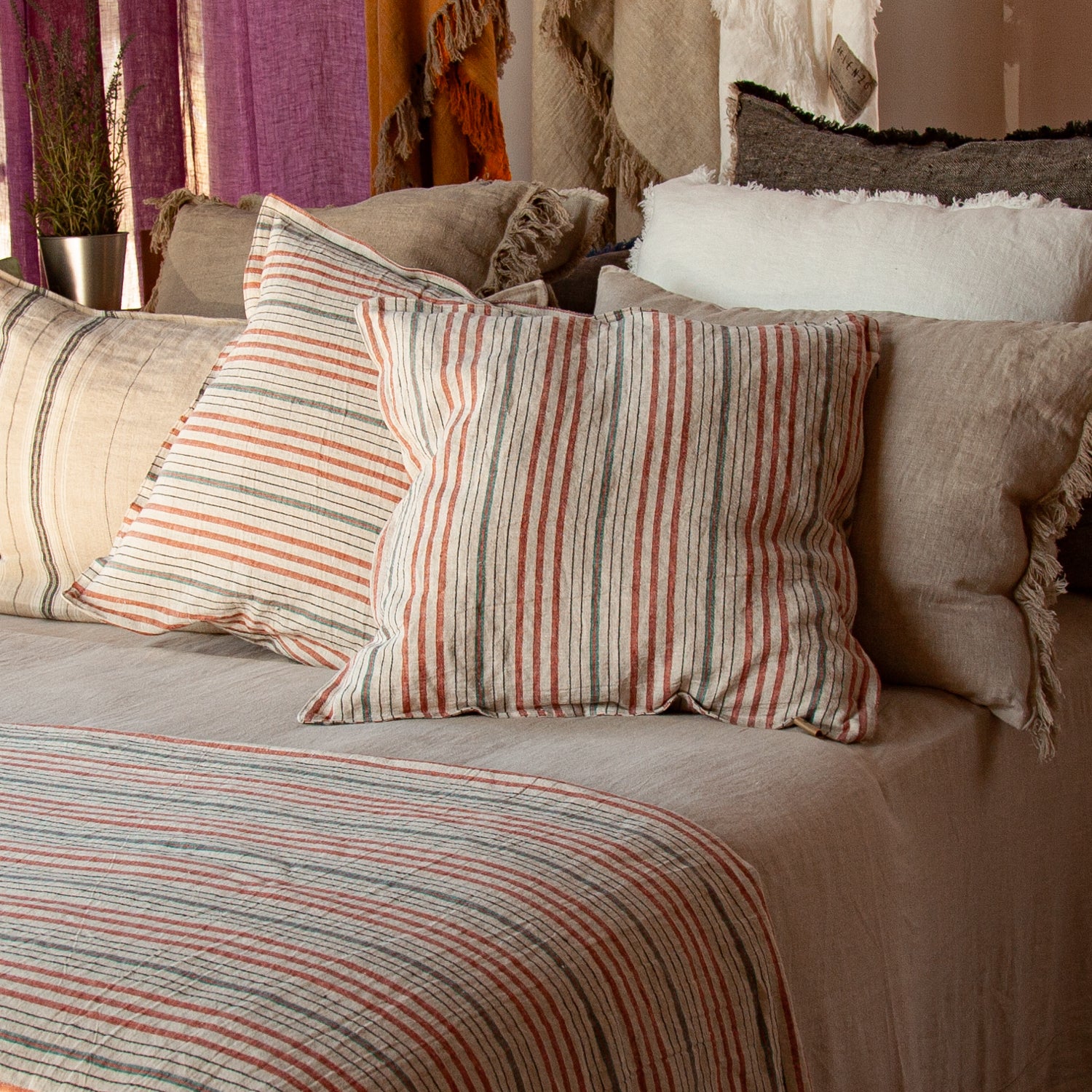 Detalle de Juego de cojines en tonos naturales con pie de cama de lino rayado y sábana de lino natural.