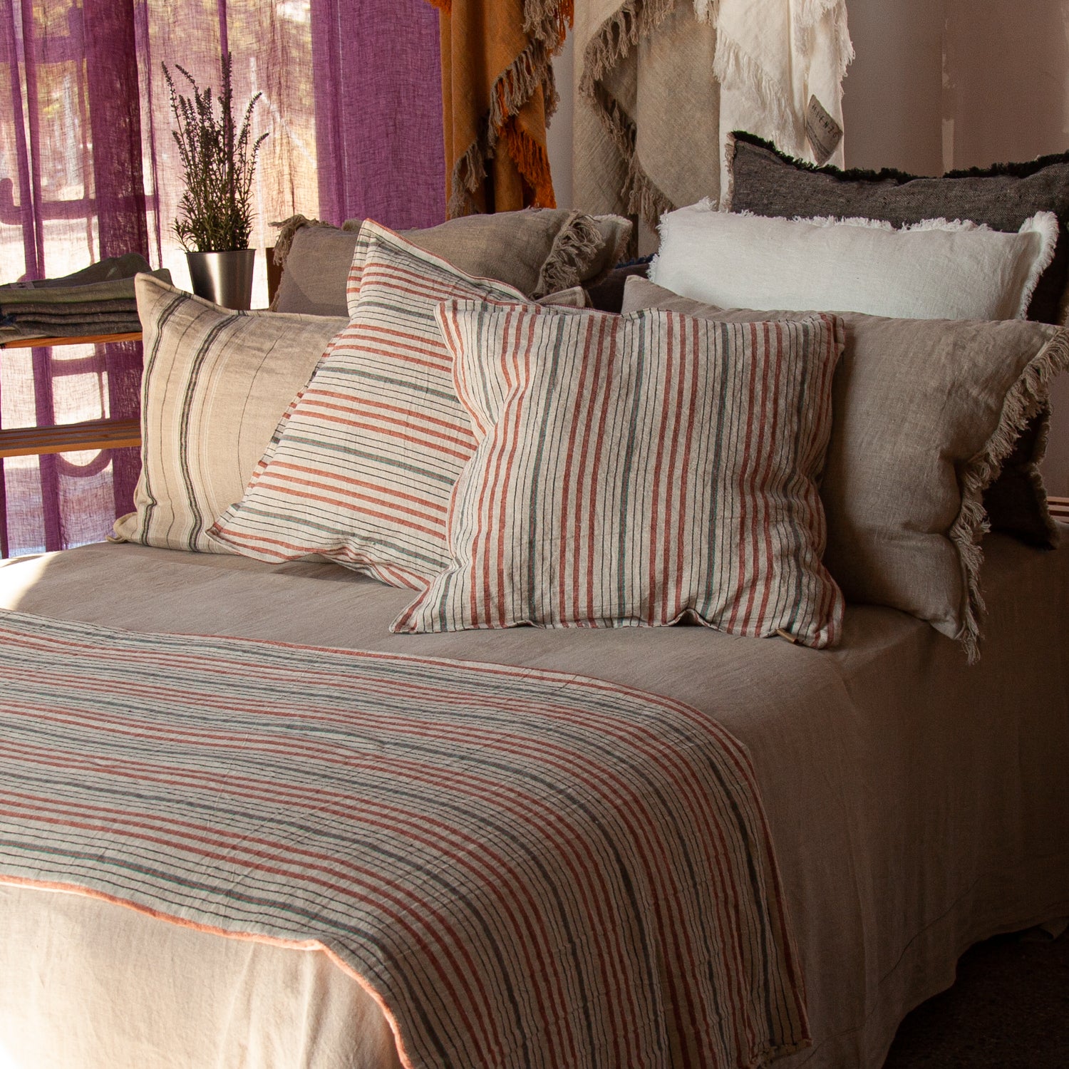 Juego de cojines en tonos naturales con pie de cama de lino rayado y sábana de lino natural.
