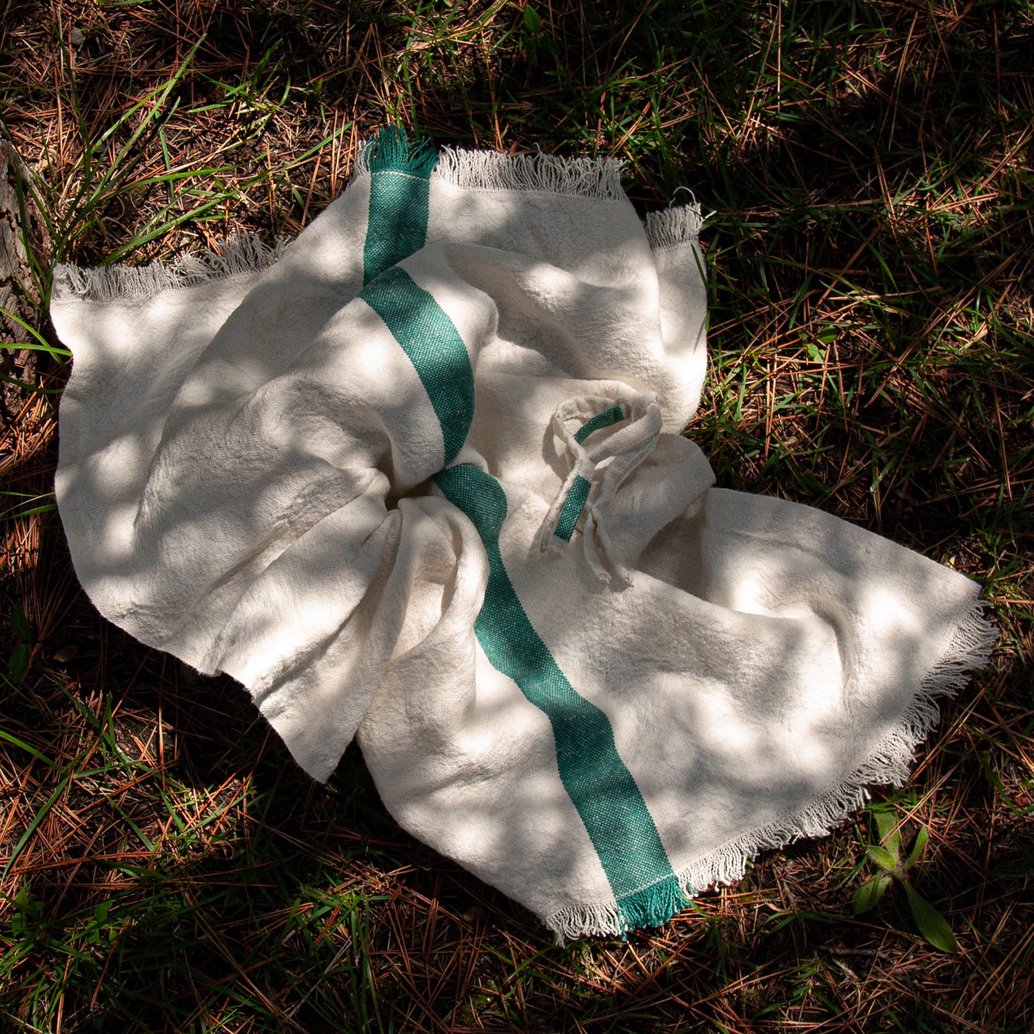 Paño de cocina de lino con raya verde sobre hierba mojada.