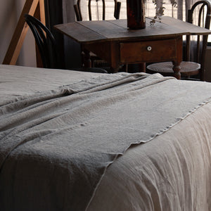 Plaid de lino natural con repulgo blanco y mesa de madera antigua.