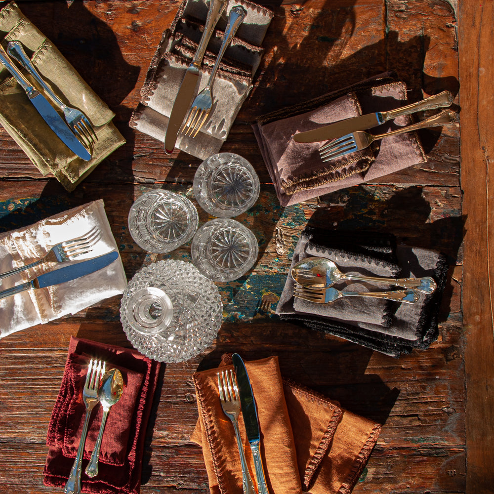 Conjunto de servilletas de lino de varios colores en mesa de madera rústica. Todo acompañado de vasos de cristal de bohemia y cubiertos de plata.