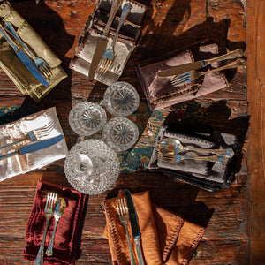Conjunto de servilletas de lino de varios colores en mesa de madera rústica. Todo acompañado de vasos de cristal de bohemia y cubiertos de plata.