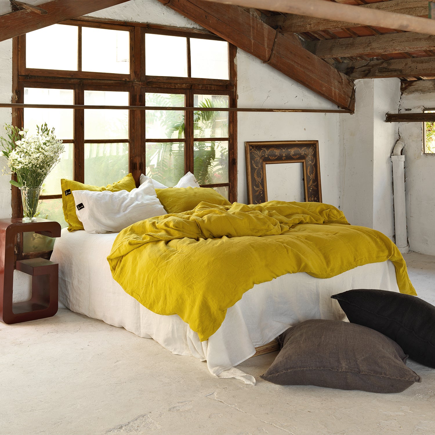 Vista general de cama con Funda nórdica de lino de color mostaza con bajera blanca y almohadas a juego.