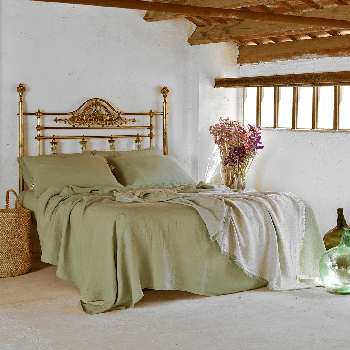 Juego de sábanas verde olivo en cama de bronce antigua. Plaid decorativo a pie de cama.