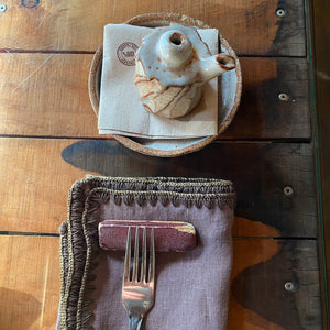 Detalle de servilleta berenjena con aceitera de ceramica.