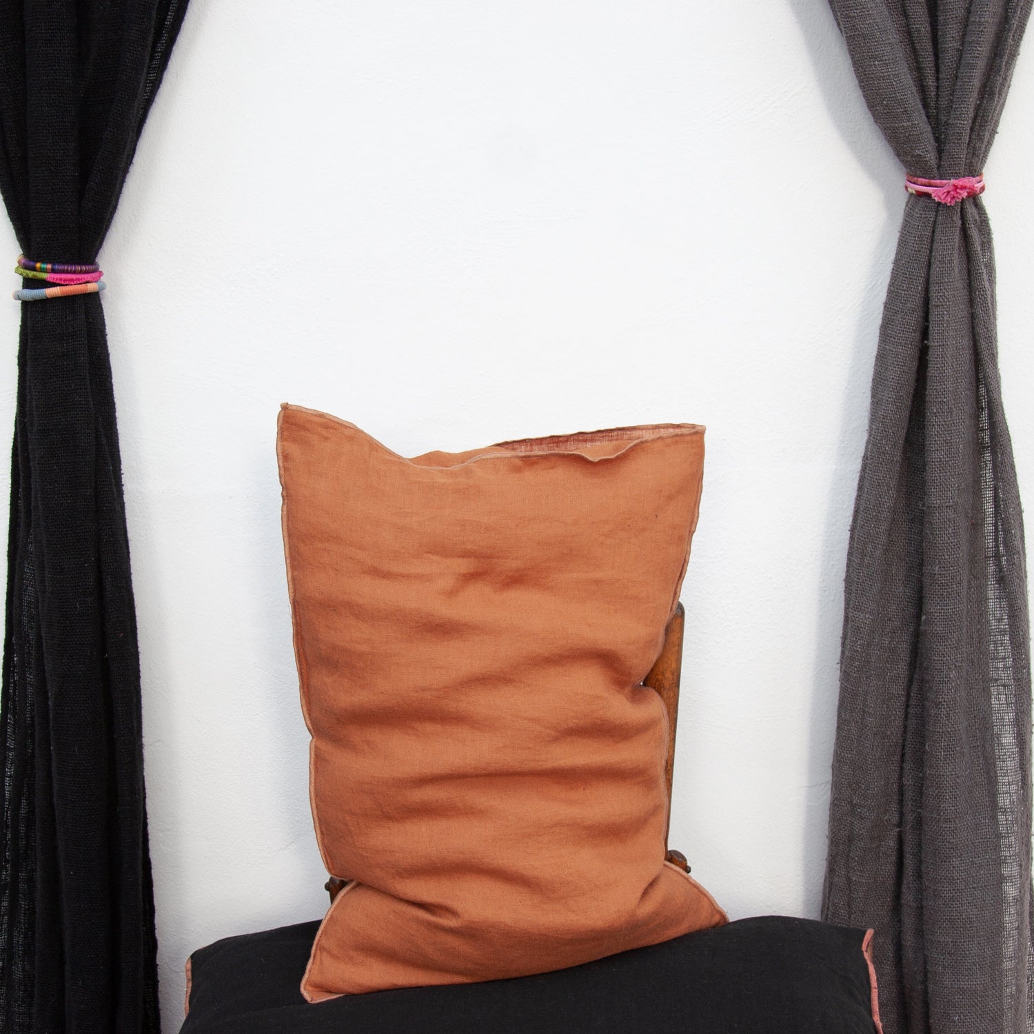 Funda de almohada de lino teja entre cortinas de lino.