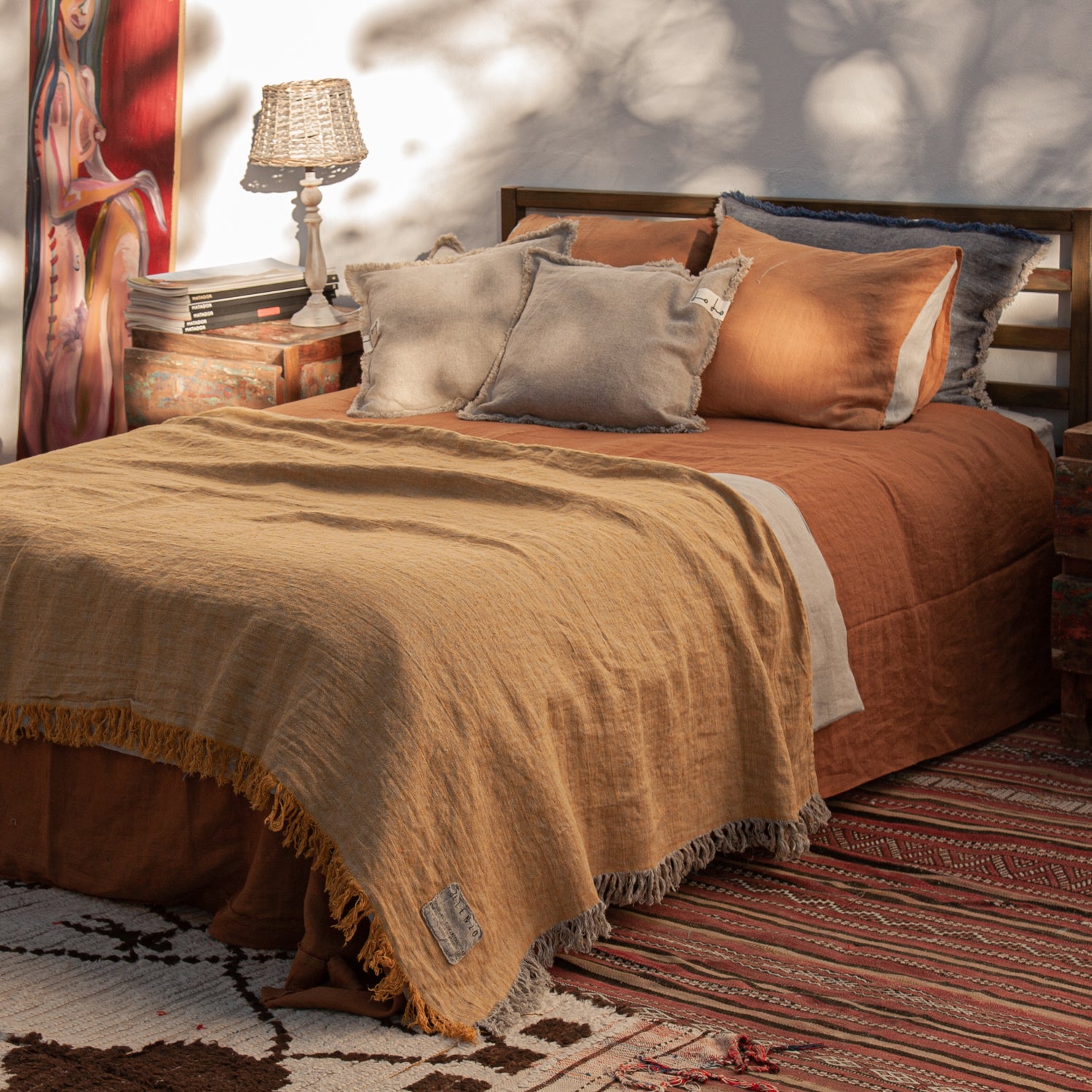 Cama de madera vestida de lino teja. Colcha mostaza y almohadones decorativos de lino rústico natural.