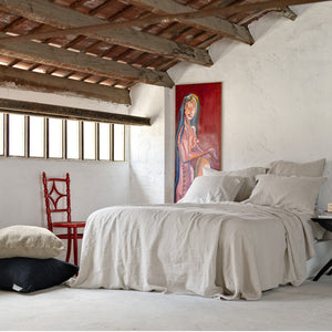 Juego de cama de lino de color piedra en habitación con techo de vista industrial y pared encalada.