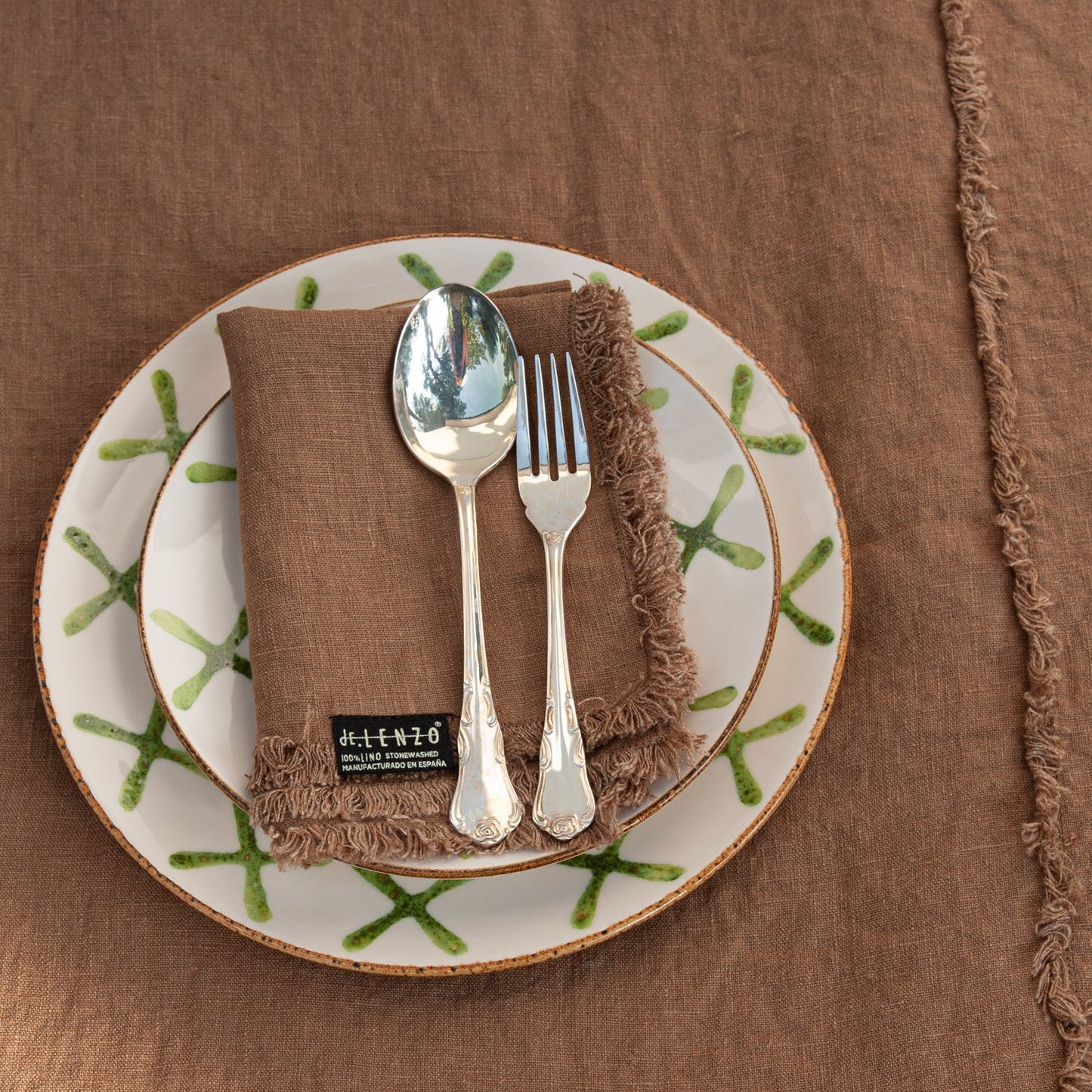 Plato verde, mantel de lino terracota y cubiertos de plata.