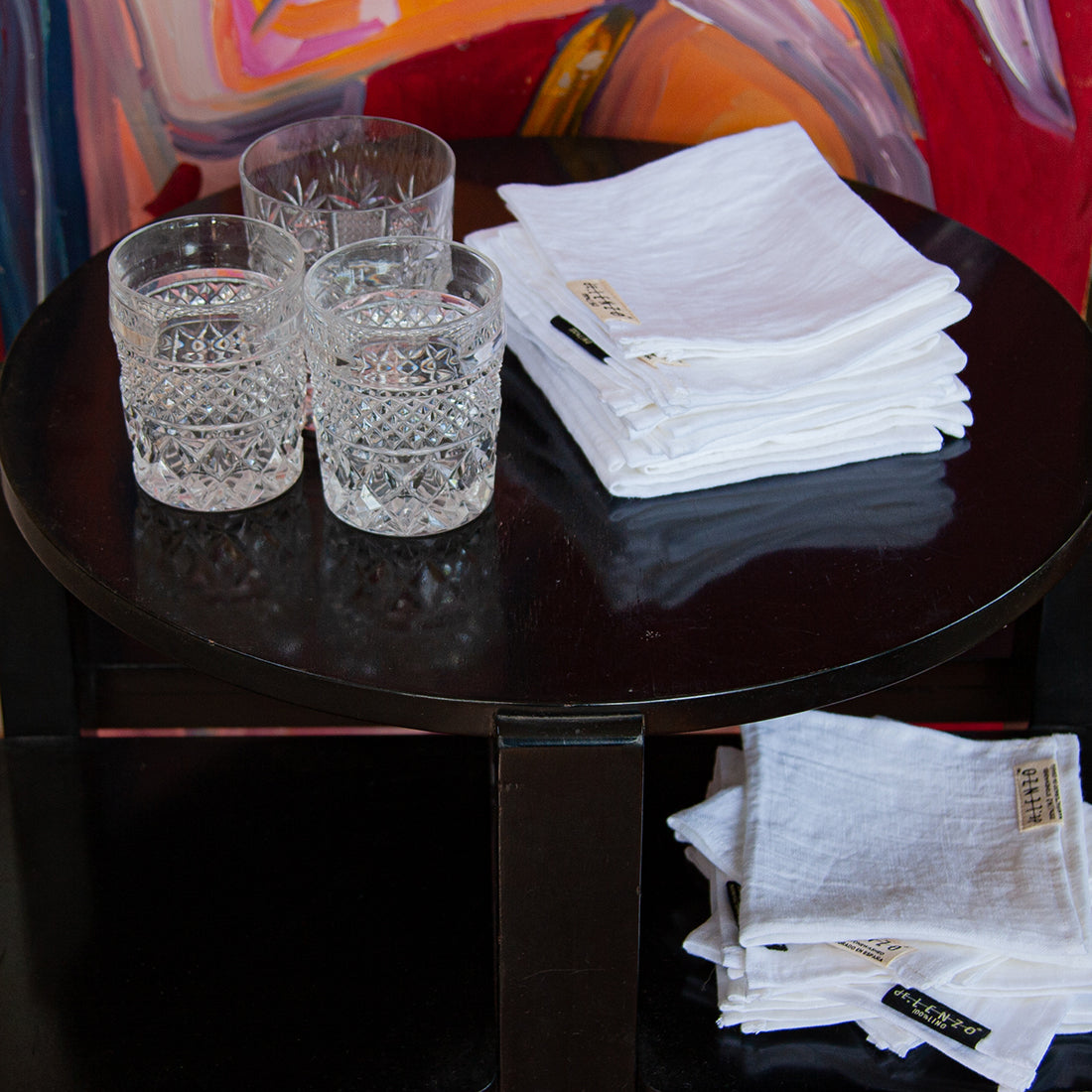 Servilletas de cóctel cuadradas sobre mesa negra y vasos de cristal de bohemia. dE.LENZO