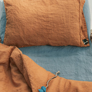 Almohada y funda nórdica de lino teja con bajera azul.