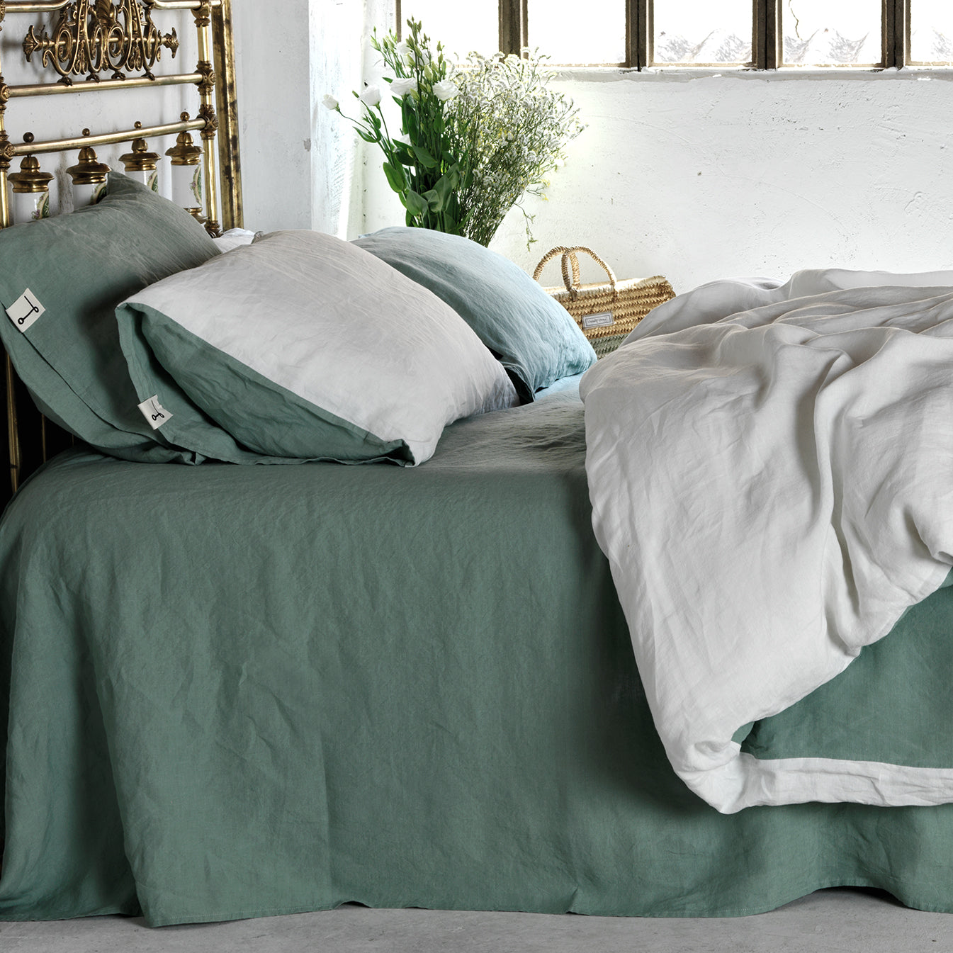 Juego de cama de lino verde menta y blanco. Habitación encalada blanca y cabezal de bronce.