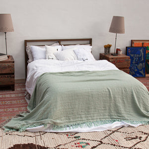 Plaid verde y sábanas de lino blanco