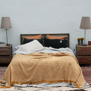 Colcha para pie de cama de lino lavado de color mostaza y cojines negros