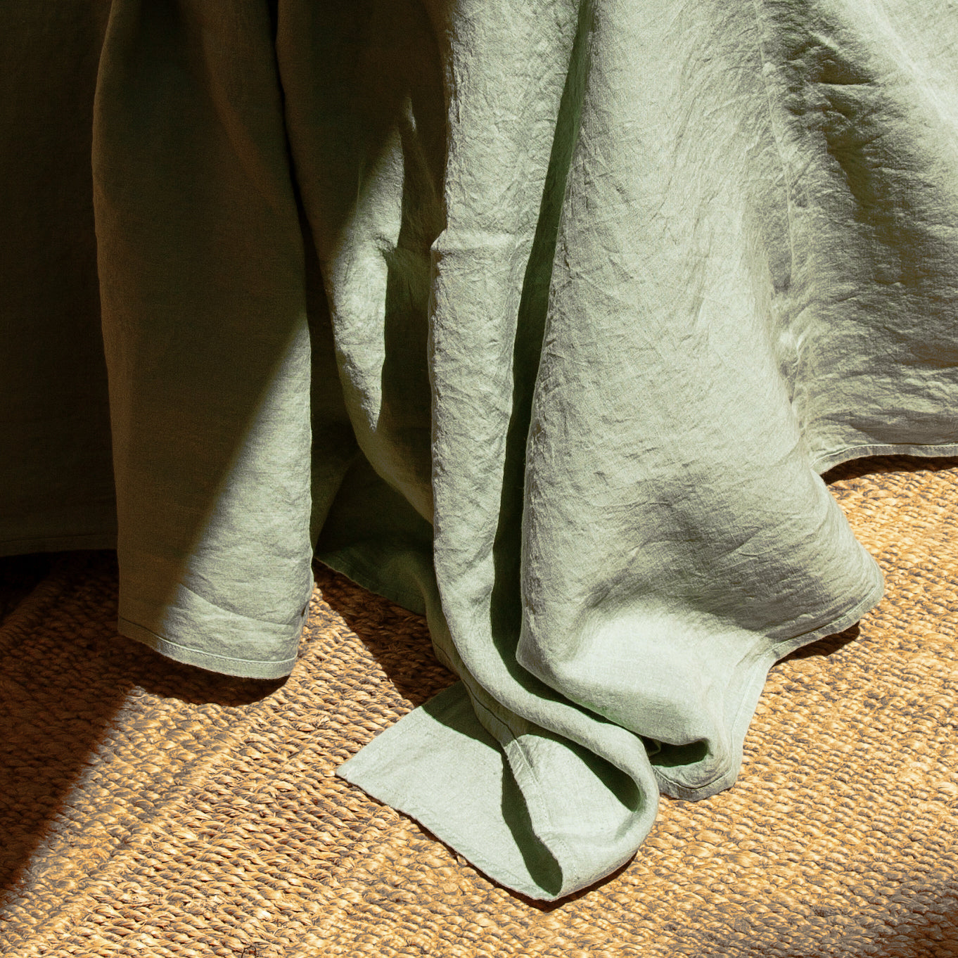 Sábana encimera de lino verde olivo. Detalle del tejido sobre alfombra de rafia.