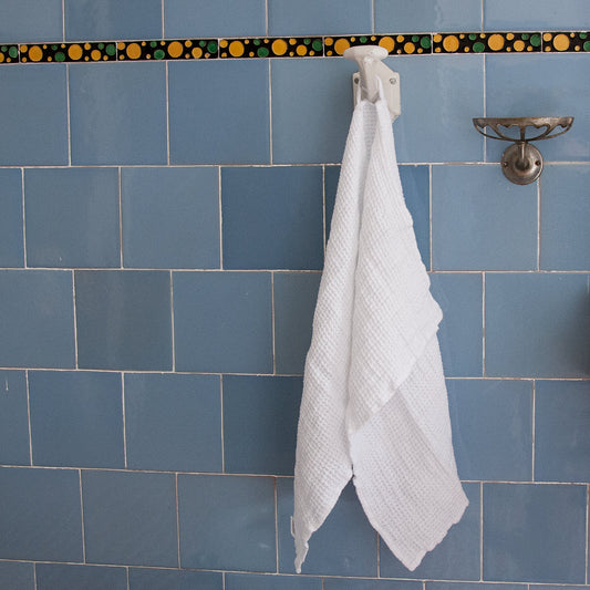 Toalla de lino blanca, colgada en baño antiguo.